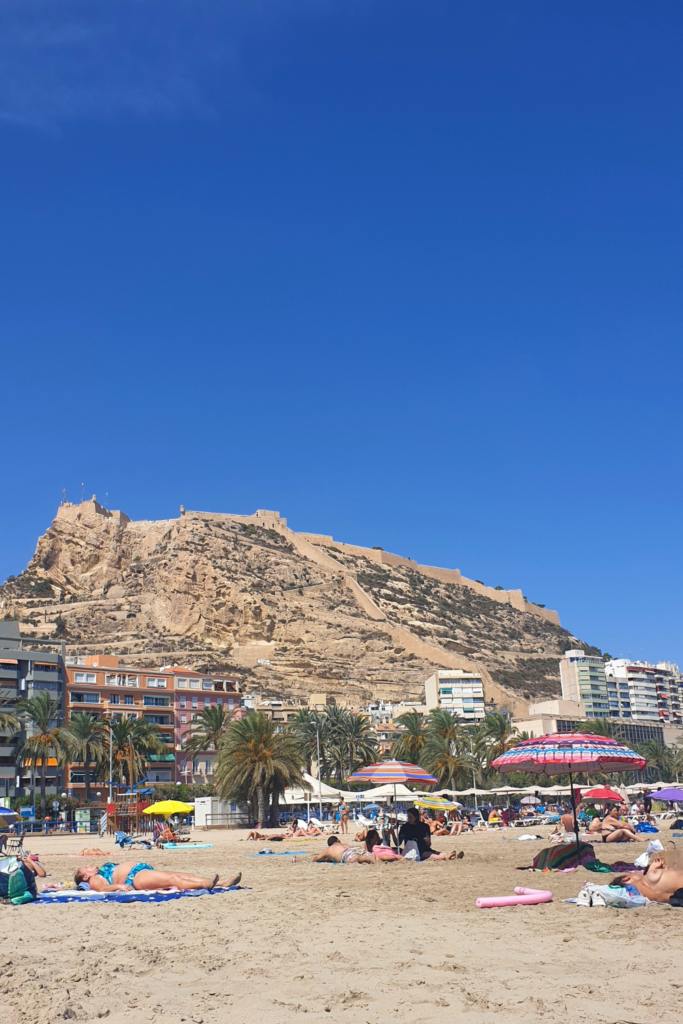 People sunbathing in Alicante, Spain at la Playa del Postiguet. View on Santa Barbara's castle.