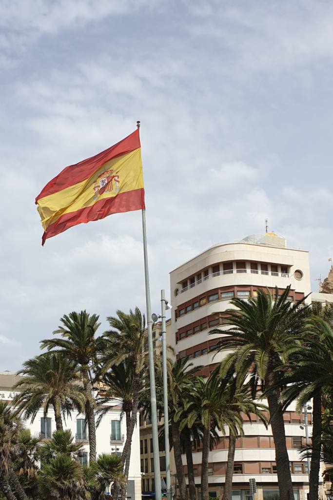 Spain flag floating in the air, surrounded by palm trees